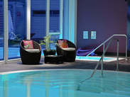 Zwei gemütliche Sessel stehen neben dem klaren Wasser des Hallenbads im Wellnessbereich des Hotel Holzapfel in Niederbayern.