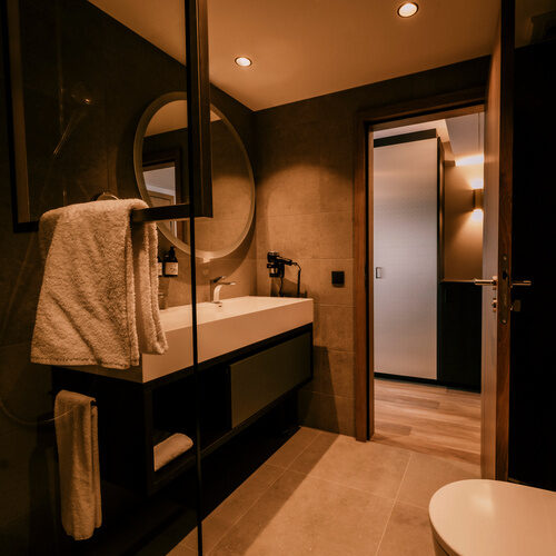 Elegant gestaltetes Badezimmer im Thermenhotel Holzapfel mit stilvollem Waschbecken, Spiegel. und WC.