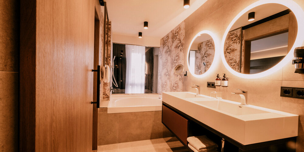 Das elegante Badezimmer in der Suite Goldrenette mit einem großen Spiegel über dem Waschbecken im Wellnesshotel Holzapfel in Bad Füssing.