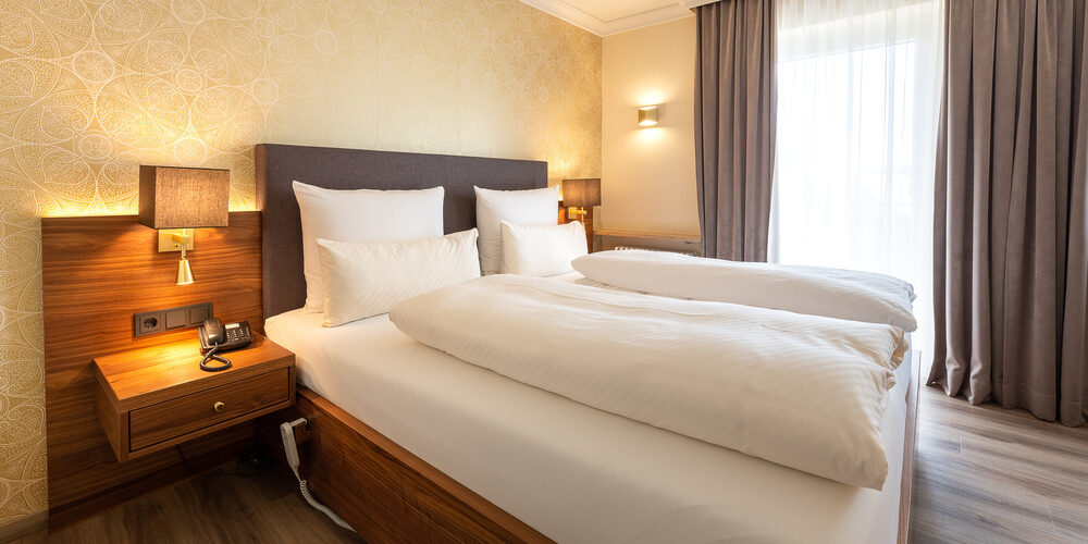 Das komfortable Doppelzimmer Standard mit klassischen Vorhängen und gemütlichen Kissen im Wellnesshotel Holzapfel Bad Füssing.