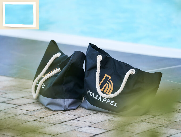 Zwei elegante Badetaschen platziert am Rande des Außenpools des Thermenhotel Holzapfel in Bad Füssing.