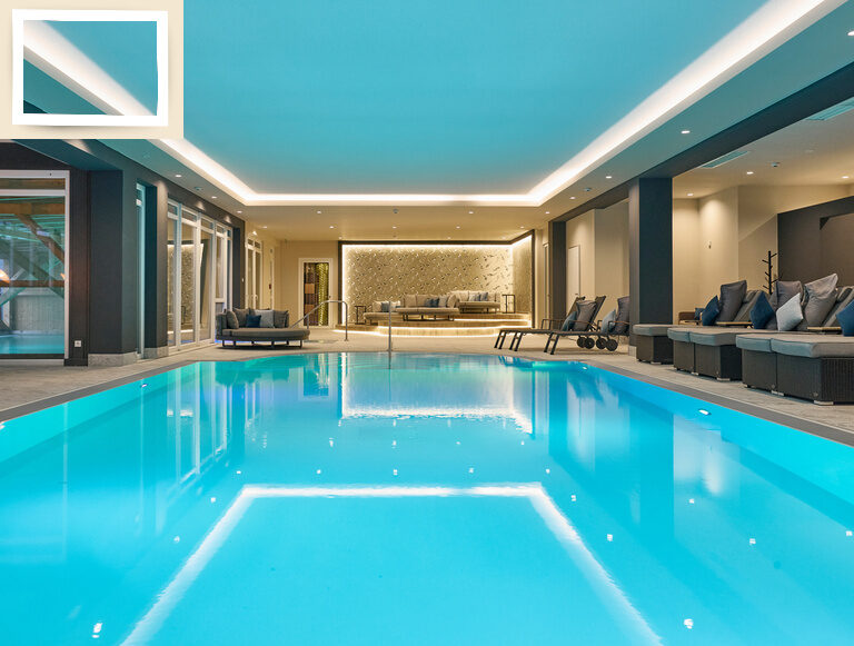 Der beleuchtete große Innenpool im Wellnessbereich des Wellnesshotels Holzapfel im Rottal lädt mit vielen Liegemöglichkeiten zum Entspannen ein.