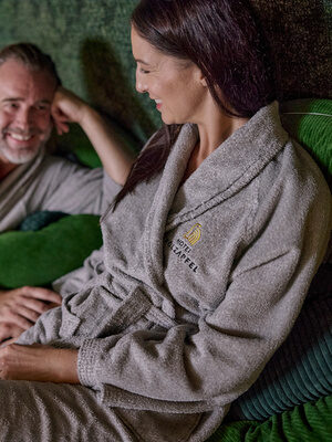 Ein Paar sitzt entspannt lächelnd auf einer Couch im Ruhebereich des Thermenhotels Holzapfel in Bayern..
