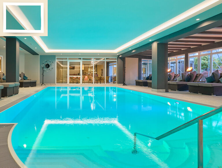 Der große beleuchtete Indoor-Swimmingpool mit gemütlichen Wellnessliegen im Hotel Holzapfel,Bad Füssing.