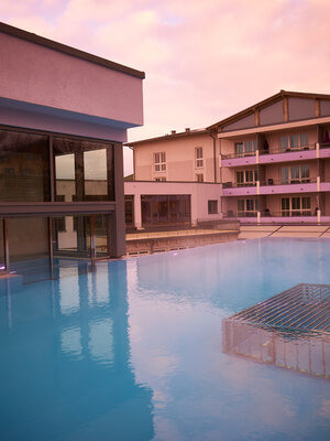 Der große Thermalwasser Außenpool am Thermalhotel Holzapfel schimmert bei der Dämmerung der Nacht.