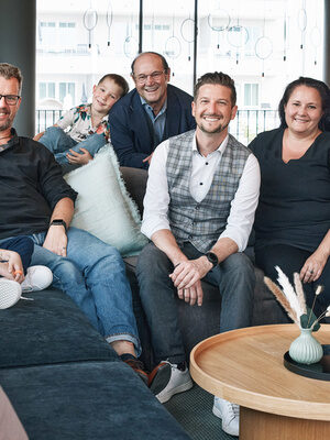 Die Gastgeberfamilie des Wellnesshotels Holzapfel sitzt zusammen lächelnd auf einer Couch