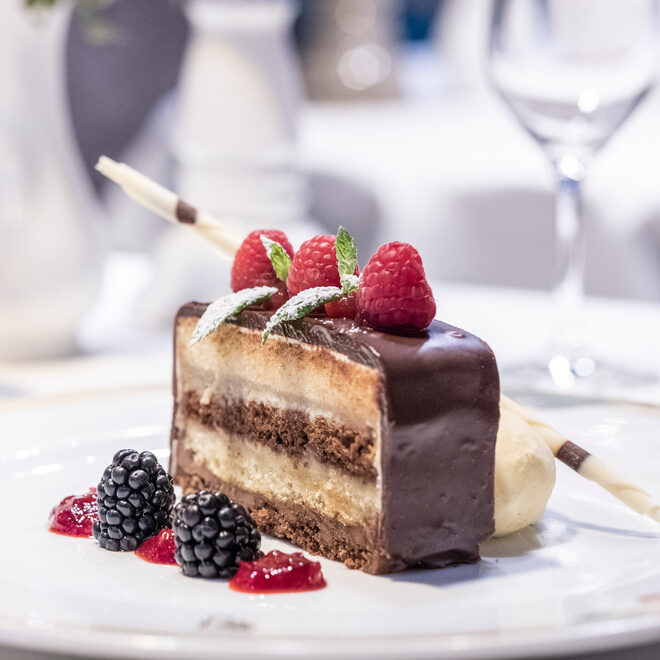 Ein Stück Schokokuchen mit Beeren als Dekoration als Dessert serviert auf einem Teller im Thermenhotel Holzapfel.
