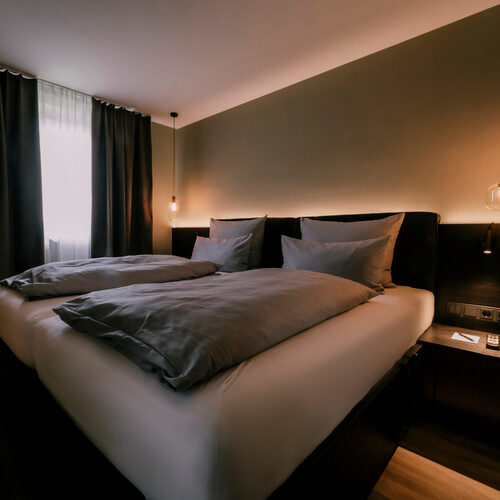 Helles Lampenlicht fällt auf das Doppelbett der Suite Jonagold im Gesundheitshotel Holzapfel bei Passau nahe einem Fernseher.