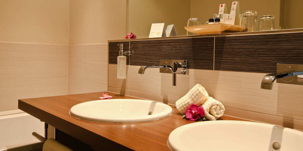 Luxuriös ausgestattetes Badezimmer im Wellnesshotel Holzapfel mit doppelten Waschbecken und einem großen Spiegel.