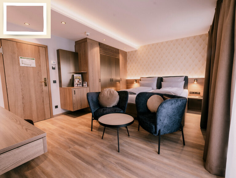 Ein einladendes Schlafzimmer im Sporthotel Holzapfel Bad Füssing, ausgestattet mit einem bequemen Doppelbett und Sesseln.
