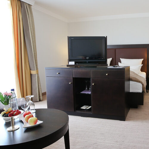 Bequemes Bett und ein Tisch mit Fernseher im Doppelzimmer Deluxe Ost des Wellnesshotel Holzapfel in Bad Füssing.