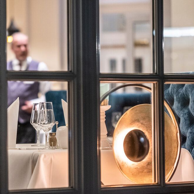 Ein Mann sitzt auf einem Stuhl im Restaurant Glockenturm des Wellnesshotels Holzapfel in Bad Füssing und blickt aus dem Fenster des Eingangsbereiches.