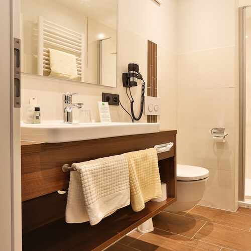 Elegantes Badezimmer mit modernen Armaturen und flauschigen Handtüchern im Thermenhotel Holzapfel, perfekt für Entspannung und Erholung im Einzelzimmer Comfort.
