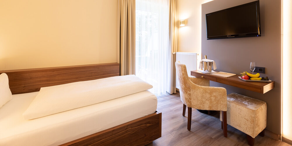 Schlafzimmer im Einzelzimmer Standart des Wellnesshotels Holzapfel mit einem komfortablen Bett, Schreibtisch und Fernseher.