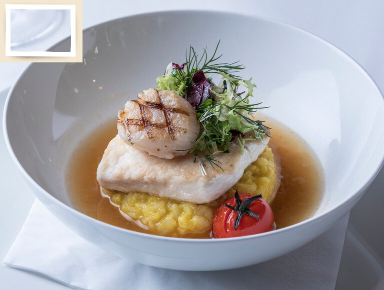 Ein Fischgericht des Gourmetrestaurants Glockenturm in einer eleganten Porzellanschüssel, serviert im Hotel Holzapfel im Rottal.