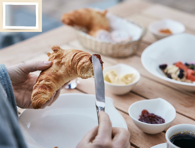Eine Person trägt  beim frühstück im Hotel Holzapfel in Bad Füssing mit einem Messer Marmelade auf ein Croisant auf.