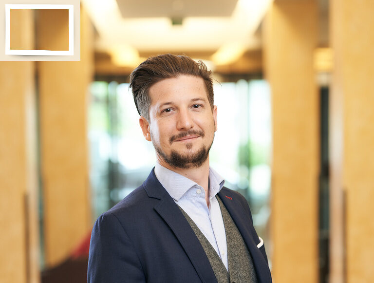 Der Gastgeber Christian Holzapfel steht im formellen Anzug mit einem Lächeln im Eingangsbereich des Hotel Holzapfel bei Bad Füssing.