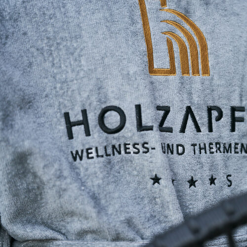 Ein Hotelgast im Thermenhotel Holzapfel in Bayern tr&auml;gt den Hotelbademantel mit dem gestickten Logo auf der Terrasse.