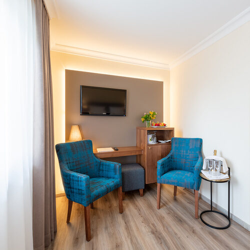 moderner Hotelzimmer Innenraum des Doppelzimmer Standard des Thermenhotel Holzapfel bei Passau mit Designerblauen Stühlen und einem großen Flachbildschirmfernseher.