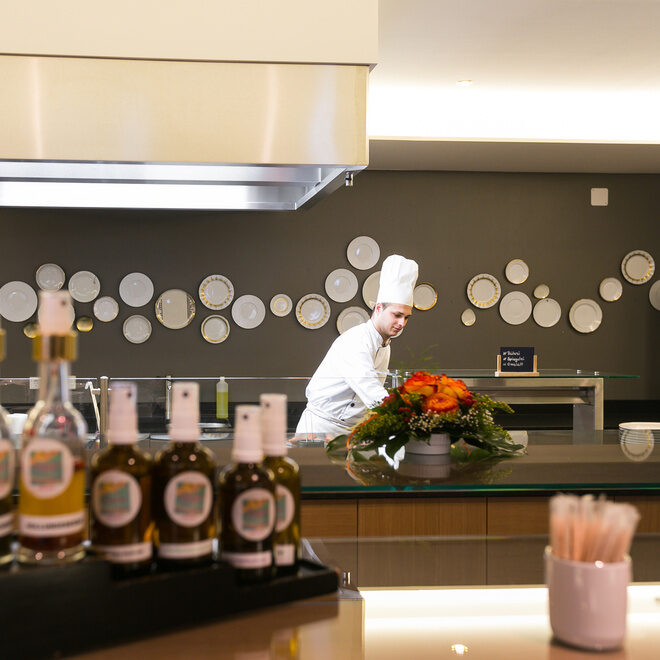 Ein Koch des Hotels Holzapfel im Rottal arbeitet mit Zutaten und Getränken auf der Theke des Buffetbereichs.