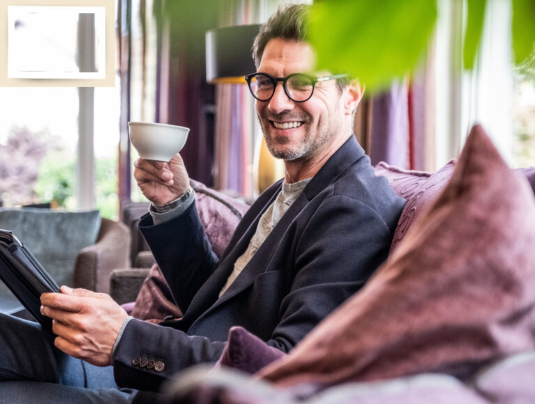 Ein Mann, komfortabel auf der Couch mit einem Tablet und einer Tasse Kaffee in der Lounge des Seminarhotel Holzapfel sitzend.