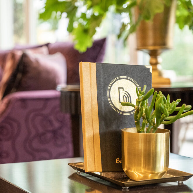 Stilvolle Sitzlounge umgeben von pflanzlichen Akzenten in luxuriösen goldenen Töpfen in der Hotellobby des Hotel Holzapfel in Niederbayern.