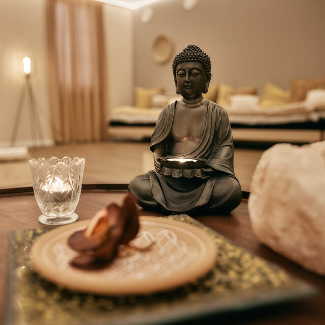 Eine Statue einer sitzenden Person in einer Meditationspose auf einem Tisch im gemütlichen Yogaraum des Fitnesshotels Holzapfel in Bad Füssing..