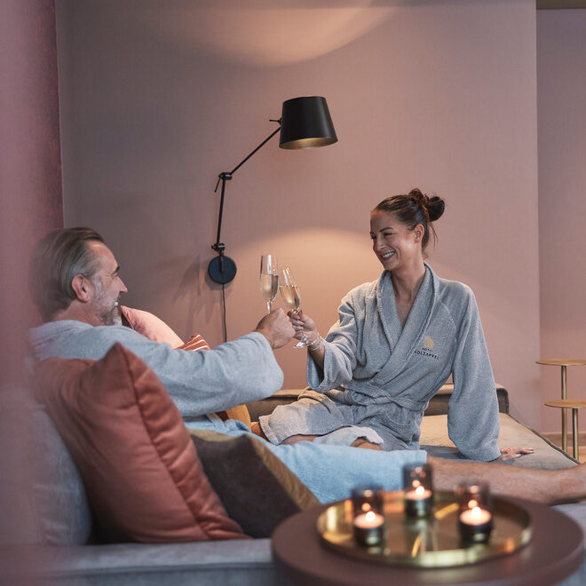 Ein Paar sitzt gemütlich mit zwei Gläsern Wein auf dem Sofa im Beautyzimmer des Wellnesshotels Holzapfel in Bad Füssing umgeben von warmem Kerzenlicht.
