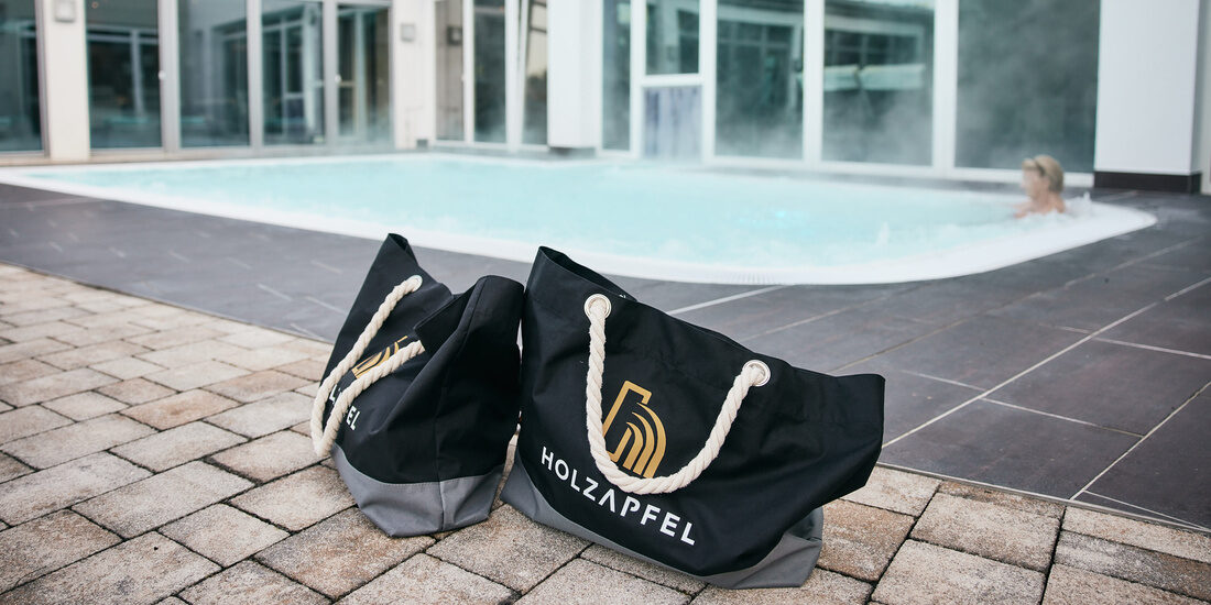 Geräumige Thermenhotel Holzapfeltaschen mit Logo liegen vor dem Aussenpool des Hotels im Rottal.