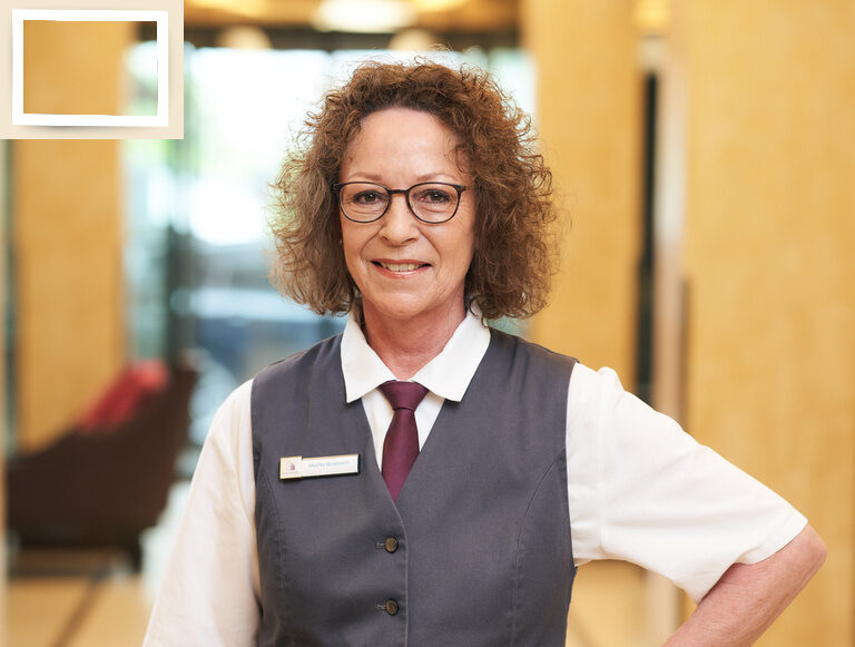 Die Service Mitarbeiterin Melitta Groebsch lächelt im 4-Sterne-Hotel Holzapfel im Rottal mit Brille und formellem Outfit.