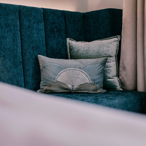 Ein gemütlicher blauer Sessel mit Zierkissen steht im stilvollen Einzelzimmer Comfort des Thermenhotels Holzapfel in Bayern.