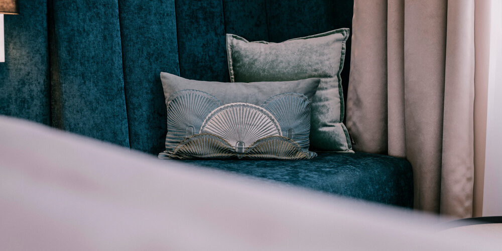 Ein gemütlicher blauer Sessel mit Zierkissen steht im stilvollen Einzelzimmer Comfort des Thermenhotels Holzapfel in Bayern.