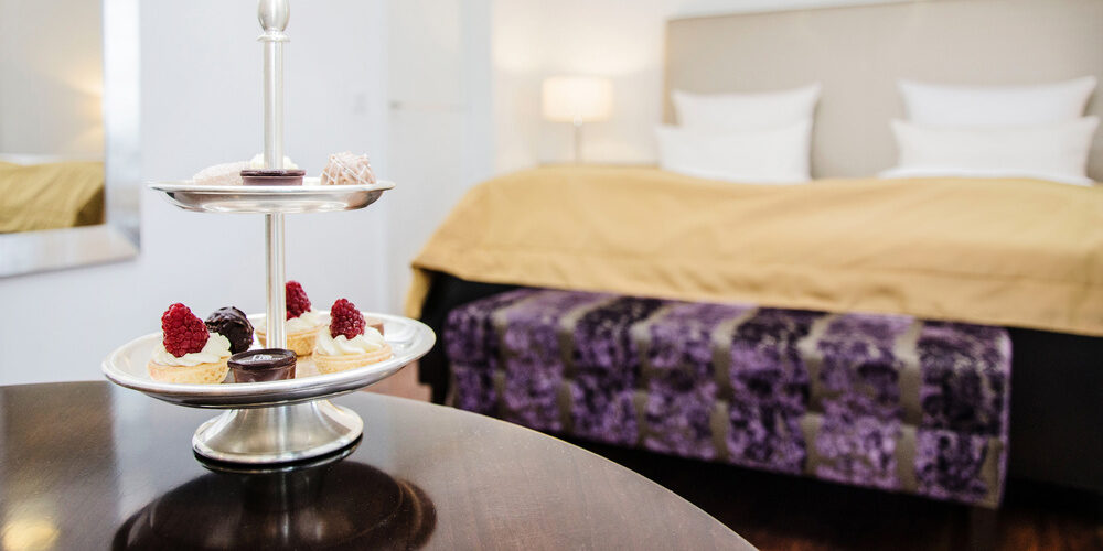Ein gedeckter Tisch mit einem süßen Dessertteller vor dem Bett in der Gala Suite des Hotel Holzapfels in Niederbayern.
