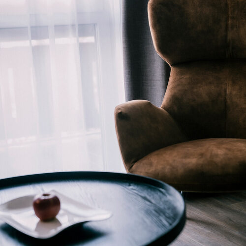 Ein gepolsterter brauner Sessel mit Beistelltisch in der Suite Golden Delicious des Wellnesshotels Holzapfel in Bad Füssing.