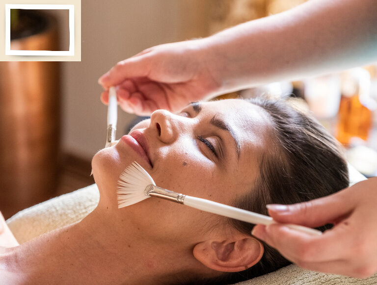 Eine Frau genießt eine entspannende Thalgo Wellnessbehandlung mit Pinseln im Kosmetikbereich des Wellnesshotel Holzapfel.