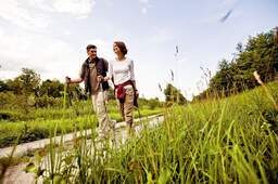 Ein Paar wandert glücklich mit Walkingstöcken durch das hohe Gras im Kur-Ort Bad Füssing.