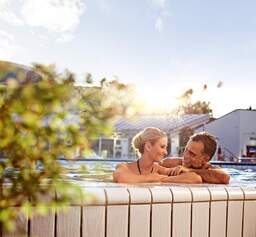 Ein Paar mit strahlenden Gesichtern genießt das sprudelnde Thermalbad in der Therme Eins Bad Füssing.