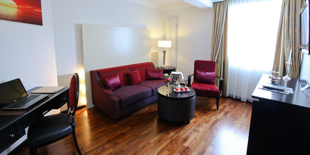 Luxuriöser Wohnbereich in der Suite Elstar, der ein einladendes Sofa und einen Schreibtisch zum Arbeiten im Thermenhotel Holzapfel in Bayern bietet.