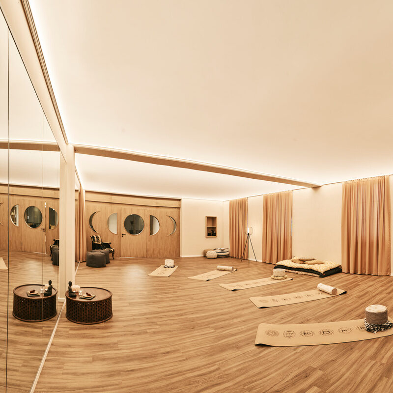 Ein heller, offener Yogaraum mit hochwertigem Holzboden, auf dem gemütliche Yogamatten liegen.