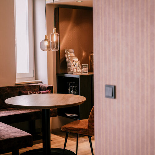 Ein eleganter Tisch mit Stühlen und luxuriösen Deckenleuchten in der Suite Goldrenette des Wellnesshotels Holzapfel.